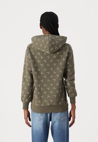 Sweatshirt à capuche vert olive avec une capuche, présentant un petit motif géométrique répétitif. Fabriqué en tissu doux avec des poignets et une bordure côtelés.