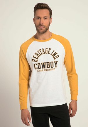 Long-sleeve t-shirt with yellow raglan sleeves and white body, featuring graphic text "HERITAGE IND. COWBOY" in dark brown. Soft cotton material.