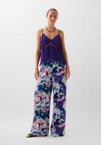 Paarse zijde camisole met kantafwerking, gecombineerd met wijde broek met een veelkleurig abstract patroon in tinten blauw, roze en wit.