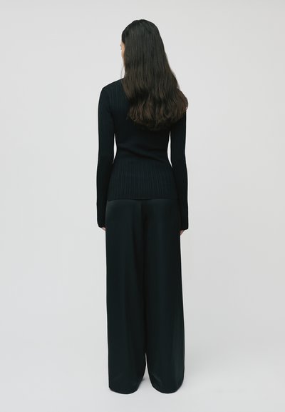 Schwarzes, ribbelndes Langarmtop kombiniert mit lockeren schwarzen Hosen, die eine glatte Textur und eine taillierte Silhouette aufweisen.