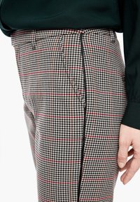 Rutig byxa med hundtandsmönster, som har svarta, vita och röda linjer. Materialet är mjukt, med slim fit och sidoficka.