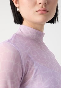 Light purple, long-sleeve top with a high collar, featuring a subtle textured pattern. Soft fabric, close-fitting design.