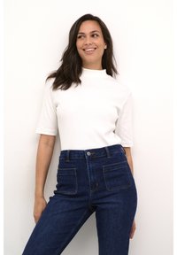 Vit ribbad polo med hög krage som matchas med mörkblå högmidjade jeans med framfickor och knappstängning. Släta texturer genomgående.