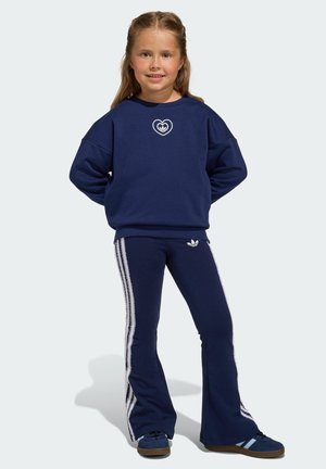 Námornícka mikina s bielym logom srdca, doplnená o námornícke rozšírené nohavice s bielymi bočnými pruhmi. Modré tenisky so svetlomodrými detailmi.