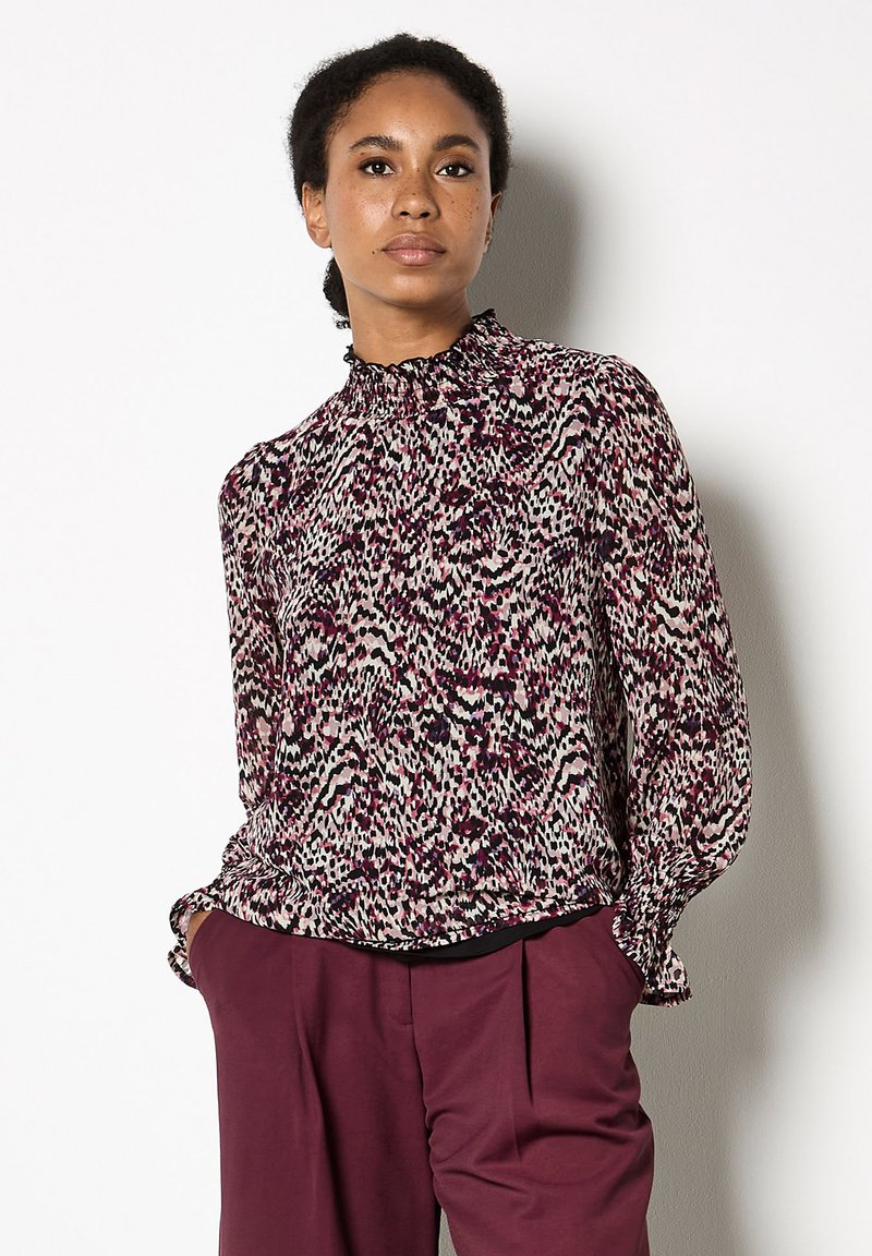 Blusa a maniche lunghe con un alto colletto arricciato, caratterizzata da un motivo astratto viola e beige. Realizzata in tessuto leggero, leggermente arricciata ai polsini.