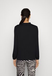 Zwarte lange mouwen top met een hoge kraag, voorzien van een zachte textuur en elastische manchetten, gecombineerd met broek met zebra-print.