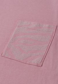 Zbliżenie różowej kieszeni z tkaniny z wzorem srebrnych ćwieków tworzących abstrakcyjne paski w zygzak.