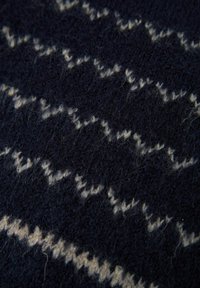 Tessuto a maglia blu navy con una superficie morbida e testurizzata, caratterizzato da un motivo a zigzag bianco, che mette in evidenza una trama densa e una leggera peluria.