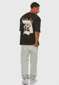 Black oversized t-shirt with floral elephant design on back. Cotton texture. Paired with light blue baggy pants and white sneakers.