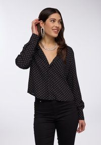 Camicia nera a maniche lunghe con un motivo a pois, design con bottoni, scollo a V profondo e taglio corto, abbinata a pantaloni neri.