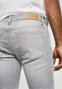 Jeans de mezclilla gris claro con un diseño ajustado. Las características incluyen dos bolsillos traseros, costuras ligeras y una etiqueta de cuero marrón en la cinturilla.