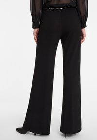 Zwarte wijde broek met een gladde textuur, voorzien van een aansluitende tailleband en subtiele studs aan de achterkant.