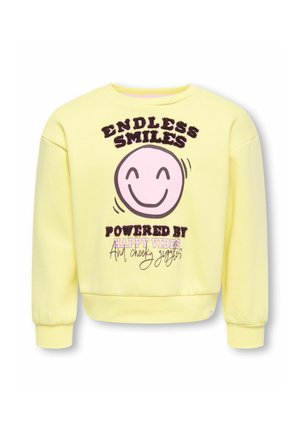 Sweat-shirt jaune avec un visage rose souriant et le texte « Sourires sans fin alimentés par des bonnes vibrations et des rires espiègles » sur le devant.