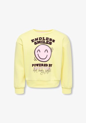 Sweat-shirt jaune avec un visage rose souriant et le texte « Sourires sans fin alimentés par des bonnes vibrations et des rires espiègles » sur le devant.