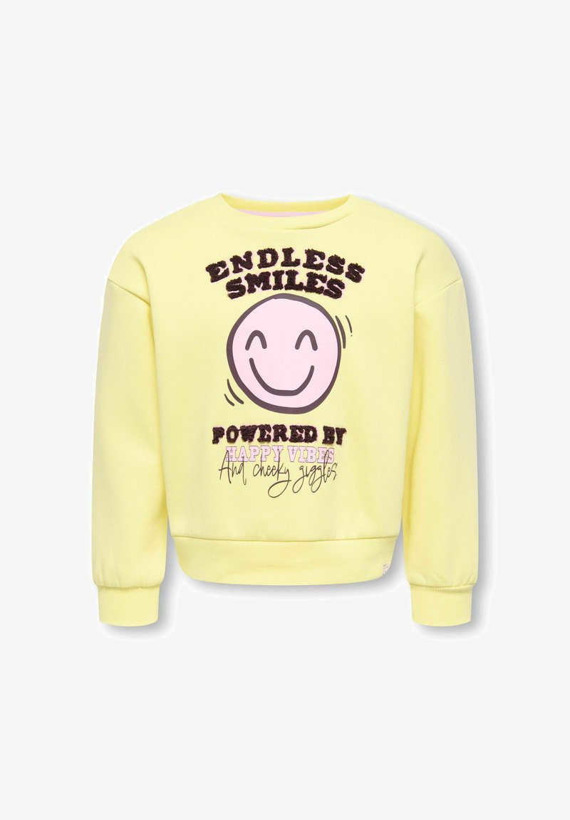 Sweat-shirt jaune avec un visage rose souriant et le texte « Sourires sans fin alimentés par des bonnes vibrations et des rires espiègles » sur le devant.