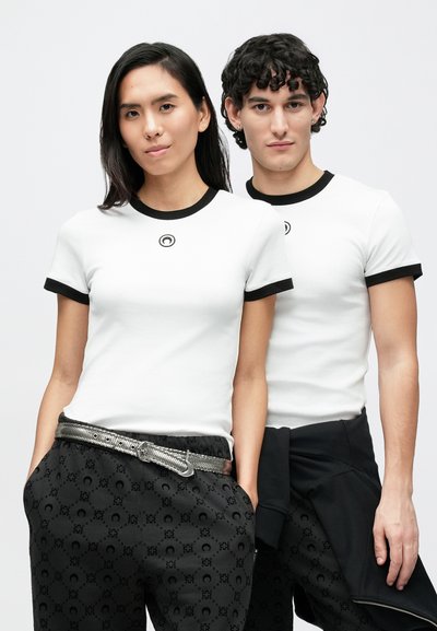 Λευκά βαμβακερά t-shirts με μαύρο ριμπ λαιμόκοψη και τελειώματα στα μανίκια. Λεπτομέρεια λογότυπου στο μπροστινό μέρος· συνδυασμένα με μαύρο παντελόνι με σχέδια και μεταλλική ζώνη.