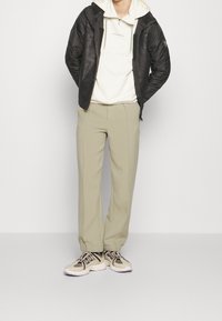 Svart puffjacka, vit zip-up hoodie, beige skräddarsydda byxor och ljusa sneakers med mörka detaljer. Ren design, neutrala färger, avslappnad look.