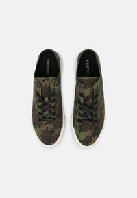 Une paire de baskets en toile montantes avec un motif camouflage vert et marron et des lacets noirs sur fond blanc.