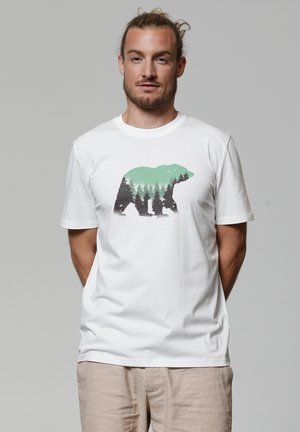 Witte katoenen t-shirt met een graphic van een silhouet van een beer, omringd door groene bomen en zwarte bosdetails, korte mouwen en een ronde hals.
