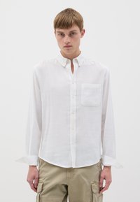 Camicia bianca a maniche lunghe realizzata in tessuto leggero, con colletto a bottone e taschino sul petto; presenta una superficie liscia e una vestibilità comoda.