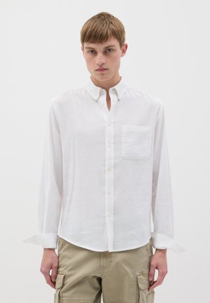Camisa blanca de manga larga hecha de tejido ligero con cuello abotonado y bolsillo en el pecho; presenta una textura suave y un corte relajado.
