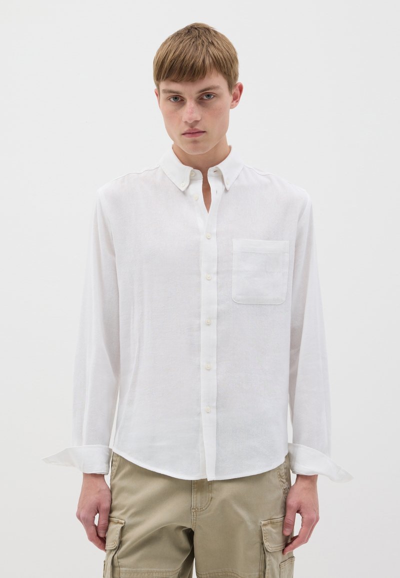 Camicia bianca a maniche lunghe realizzata in tessuto leggero, con colletto a bottone e taschino sul petto; presenta una superficie liscia e una vestibilità comoda.