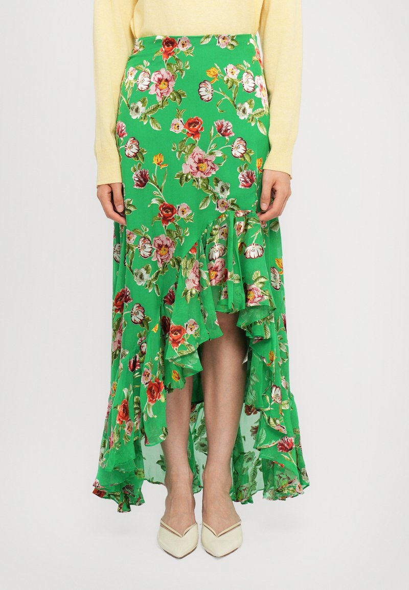 Longo gonna floreale in tessuto verde con orlo arricciato, caratterizzato da una combinazione di fiori rossi, rosa e gialli; abbinata a tacchi color crema.