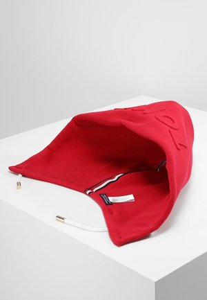 Capucha de tela roja con cordones blancos que tienen puntas doradas, etiqueta interior visible y texto bordado en el lado superior.