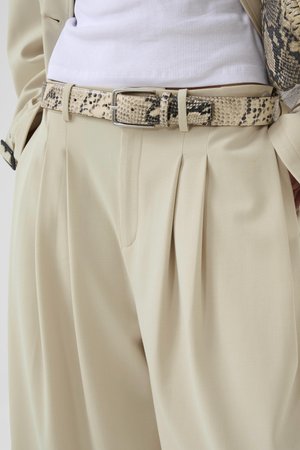 Beżowe, plisowane spodnie z wysokim stanem, z teksturowanym paskiem w deseń węża oraz biała prążkowana bluzka wsunięta do środka.