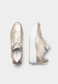 Sneaker metallic oro con una texture liscia, lacci bianchi, zip decorativa e una suola spessa bianca. Punta arrotondata e motivo a fiocco sul tallone.