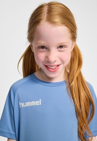 Ljusblå sportskjorta med korta ärmar och rund halsringning. Har en vit "hummel"-logotyp på framsidan. Slät, syntetisk material.