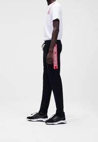 Vit t-shirt med ficka, svarta sweatpants med röd sidremsor och text, samt svarta sportskor med vita sulor.