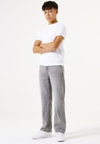 Camiseta blanca de manga corta combinada con jeans rectos de color gris claro y zapatillas blancas; diseño minimalista con un corte relajado y sin patrones visibles.
