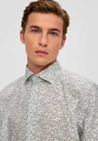 Hellfarbendes Hemd mit geometrischem schwarzen Muster, Button-Down-Kragen und glattem, leichtem Stoff.