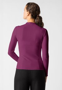 Dlouhý rukáv vršek v tmavě fialovém žebrovaném materiálu, s vykrojeným výstřihem a přiléhavým střihem, kombinovaný s černými spodními částmi.