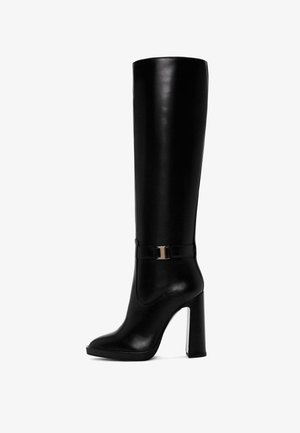 Botas de cuero negras hasta la rodilla con punta afilada, tacón alto y robusto, y detalle de hebilla con acento dorado en el tobillo. Textura suave en toda su superficie.