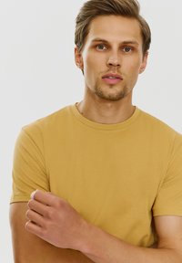 Żółta bawełniana koszulka z okrągłym dekoltem i krótkimi rękawami, zaprezentowana na modelu męskim. Gładka tekstura i dopasowany krój.