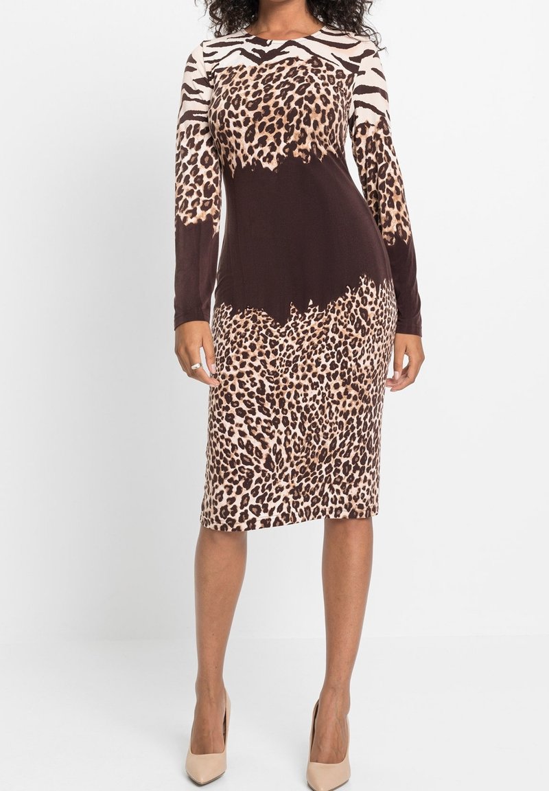 Femme portant une robe ajustée longueur genou avec imprimés animaliers mélangés et manches longues, associée à des chaussures à talons hauts beiges.