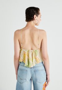 Blomstertrykt crop top i gul, grønn og rosa med volangkant, tynne stropper og åpen rygg, parret med lyseblå høytlivsjeans.