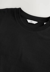 Zwarte katoenen T-shirt met een ronde hals, vlakke naden en een zichtbaar "NEXT" label binnenin de kraag. Gladde textuur, reguliere pasvorm.
