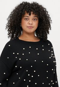 Pulover negru din tricot, decorat cu perle împrăștiate. Designul include un croi lejer și un guler rotund.