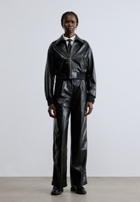 Svart läderjacka med kortare design, dragkedja och ribbstickade muddars, kombinerad med högmidjade, vida byxor i matchande läder.