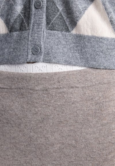 Cardigan gri cu nasturi, cu model de triunghiuri, purtat peste un top alb din tricot și fustă din lână bej, prezentat într-un prim-plan.