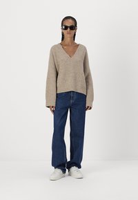 Pulover bej tricotat cu decolteu în V și mâneci lungi, asortat cu blugi dark blue, largi și adidași albi. Design simplu, texturat.