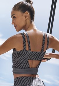 Grauer und schwarzer Sport-BH mit Zebra-Streifen und einem einzigartigen Rückendesign mit breiten Trägern und Ausschnitten. Glattes, dehnbares Material.