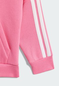 Sudadera rosa con rayas blancas en las mangas, puños de canalé y un tejido suave y texturizado. Incluye un bolsillo frontal.