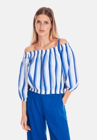 Off-the-shoulder blouse with blue and white vertical stripes, balloon sleeves, and elastic hem. Paired with blue pants.