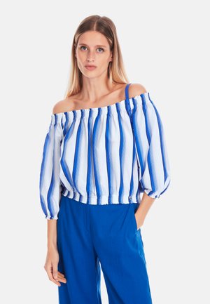 Off-shoulder Bluse mit blauen und weißen vertikalen Streifen, Ballonärmeln und elastischem Saum. Kombiniert mit blauen Hosen.