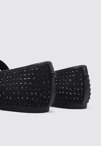 Black shoes with a smooth texture, featuring a perforated design. Rounded shape and flat soles; small accents near the heel.