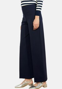 Tumesinised laia säärega püksid, millel on sile tekstuur, kõrge vöökoht ja puhas siluett, kombineeritud hõbedaste lamedate kingadega.